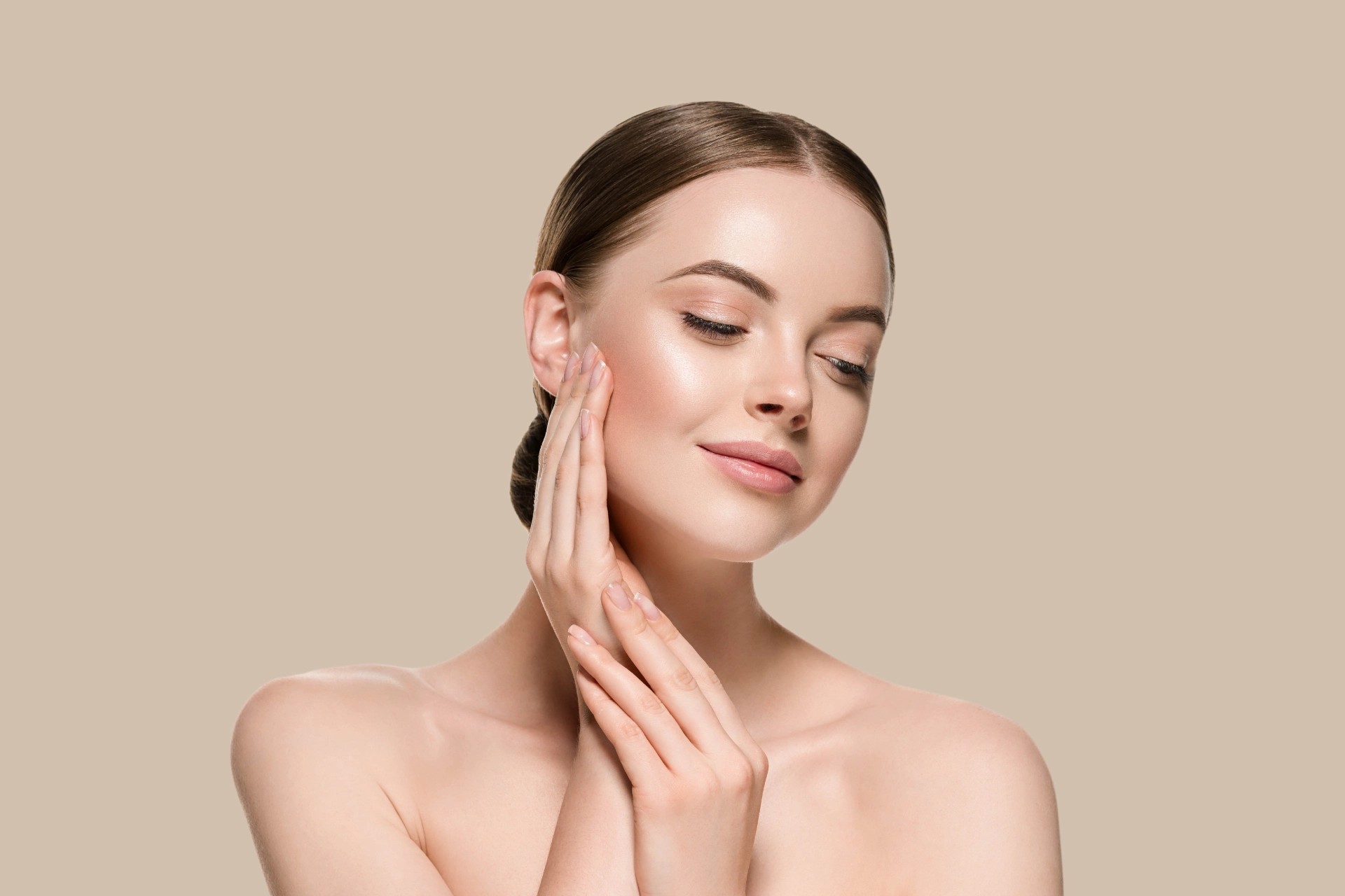 A woman with clear, bare skin rests her fingertips against her cheek and jaw in front of a plain warm-beige background